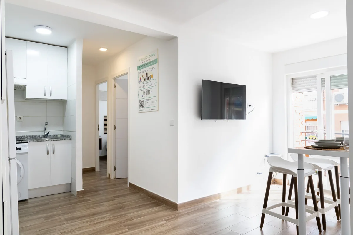 Zona común del proyecto Nardo con cocina, mesa y televisión junto a la ventana.